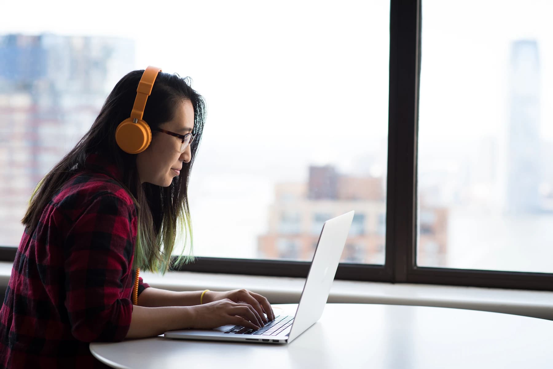A web professional working at a laptop beside a bright studio window.